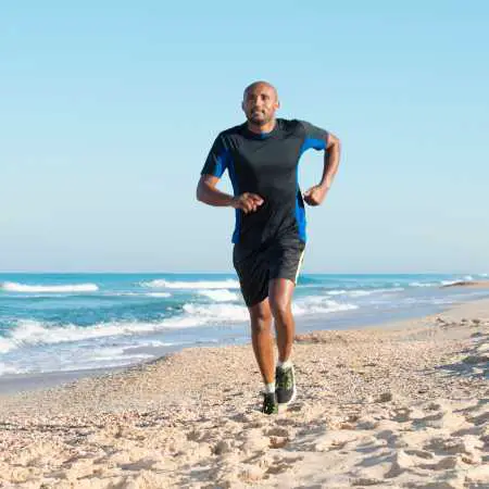 Man wearing a short sleeve shirt and shorts while running on the beach 