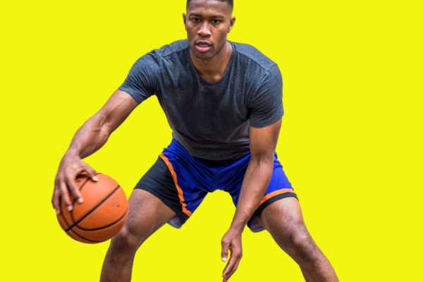 A photo of a basketball player against a yellow background. Athlete is wearing a compression shirt and dribbling the ball