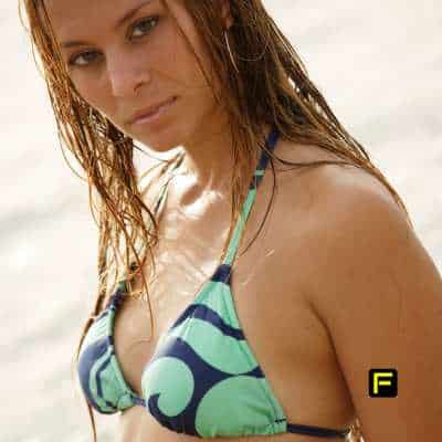 A confident woman with wet hair wearing a patterned bikini top, standing near the beach. The image conveys natural beauty, self-care, and summer confidence, ideal for content related to bust firming, skincare, and body enhancement.