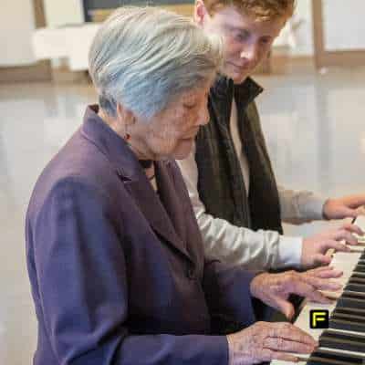 Senior woman playing piano with a younger man, representing cognitive sharpness, memory retention, and the benefits of creatine for brain health in seniors.