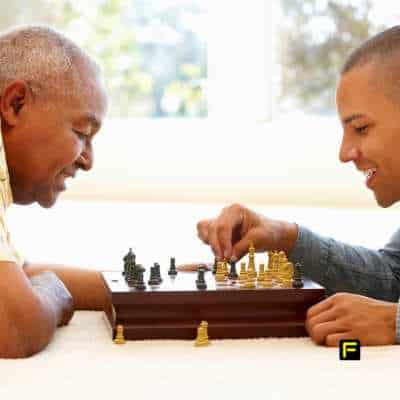 Smiling senior man playing chess with a younger man, symbolizing cognitive sharpness, strategic thinking, and the benefits of creatine for brain health in seniors.