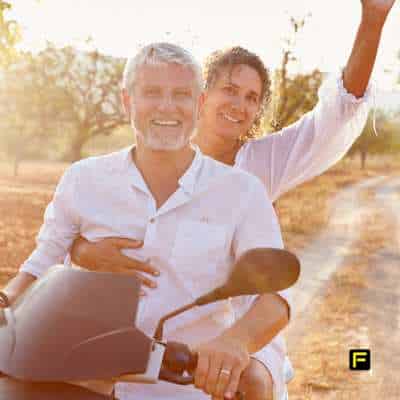 Mature couple riding a scooter near a park representing active aging and the benefits of creatine for seniors in maintaining mobility, strength, and overall well-being.