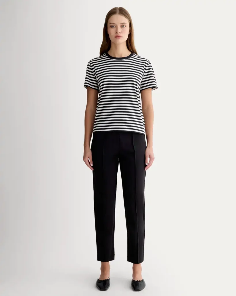 Best Wide Leg Pants for Women Over 50: Stylish, Comfortable, Flattering Options for 2025 16 Woman wearing black Everlane The Dream Pant with a slim fit and ankle-length cut, paired with a black and white striped t-shirt and black flats, standing against a plain white background.